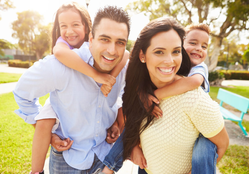 Parents Giving Children Piggyback Ride In Garden